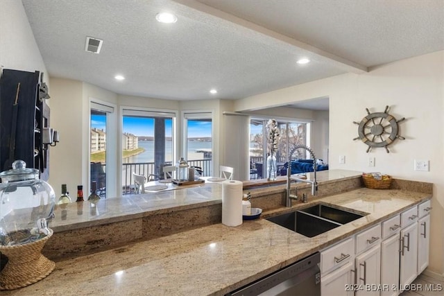 kitchen featuring sink, a water view, stainless steel dishwasher, and a textured ceiling