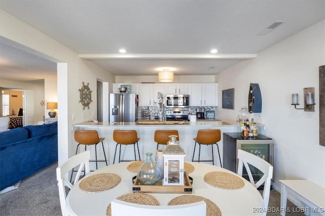 kitchen featuring backsplash, white cabinets, a kitchen breakfast bar, appliances with stainless steel finishes, and kitchen peninsula