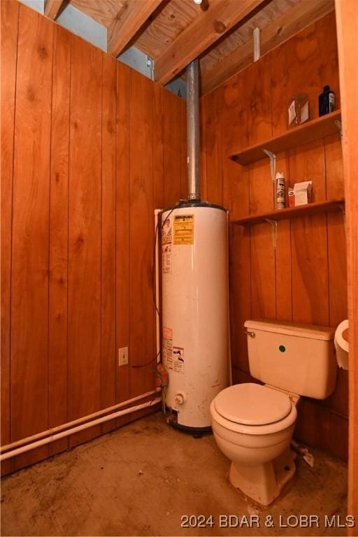 bathroom featuring water heater, wood walls, and toilet