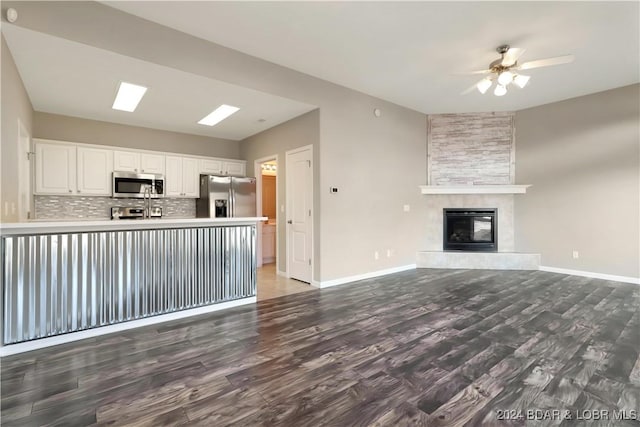 unfurnished living room featuring a tile fireplace, ceiling fan, and dark wood-type flooring