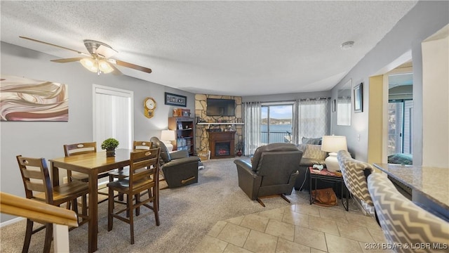 living room with light carpet, a textured ceiling, a stone fireplace, and ceiling fan