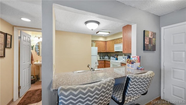 kitchen with white appliances, sink, a textured ceiling, light tile patterned flooring, and kitchen peninsula