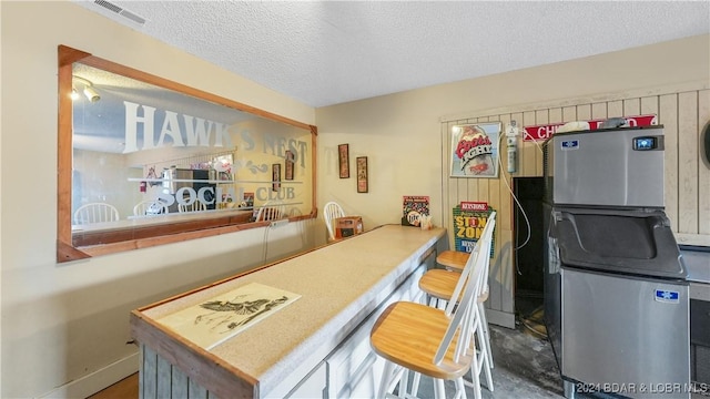 kitchen featuring stainless steel fridge, a kitchen bar, and a textured ceiling