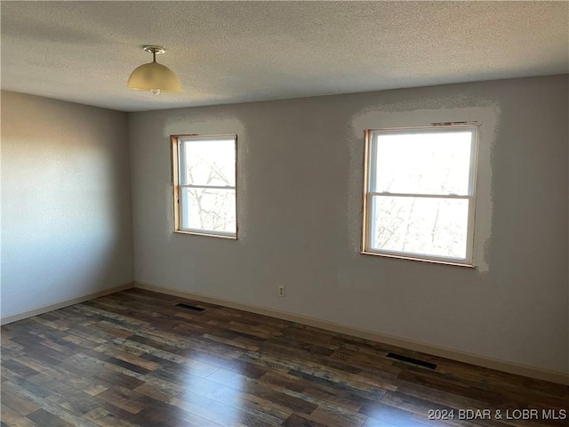 spare room with a textured ceiling, dark wood-type flooring, and a healthy amount of sunlight