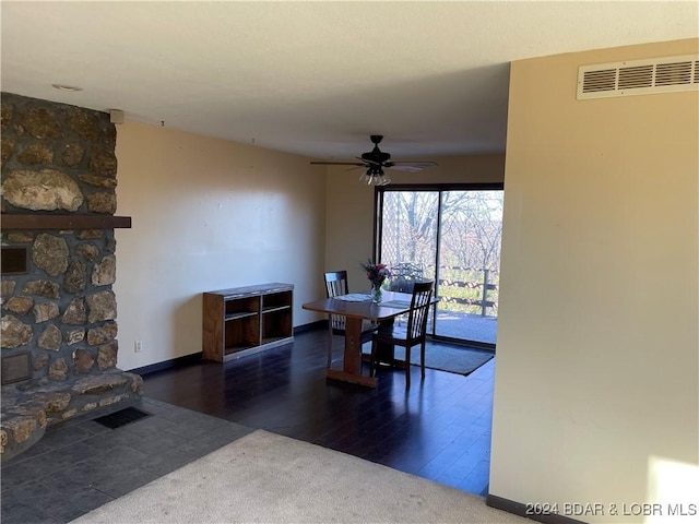 dining room featuring ceiling fan, a fireplace, and dark wood-type flooring