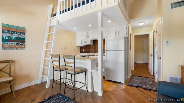 kitchen with white appliances, wood finished floors, visible vents, white cabinetry, and a kitchen breakfast bar