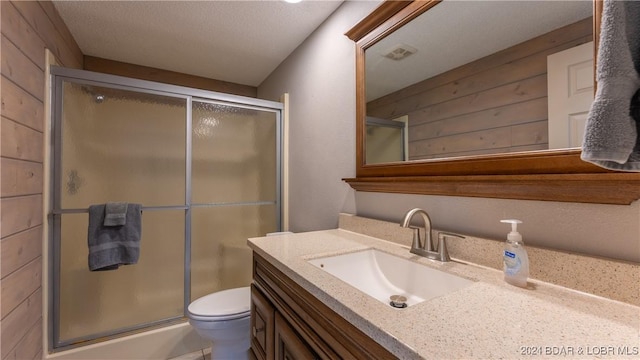 bathroom featuring vanity, wooden walls, toilet, a textured ceiling, and walk in shower