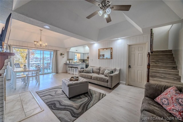 living room featuring light wood-type flooring, ceiling fan with notable chandelier, vaulted ceiling, and wood walls