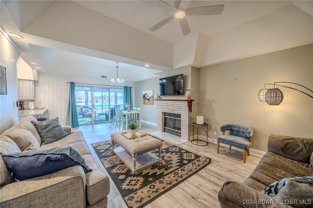 living room featuring a fireplace, wooden walls, light hardwood / wood-style flooring, and ceiling fan with notable chandelier