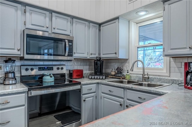 kitchen featuring backsplash, gray cabinetry, sink, and stainless steel appliances