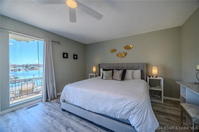 bedroom with ceiling fan, a water view, wood-type flooring, and multiple windows