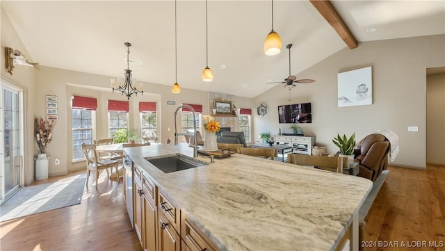 kitchen with ceiling fan with notable chandelier, sink, a fireplace, vaulted ceiling with beams, and hanging light fixtures