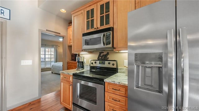 kitchen featuring light wood-type flooring, light stone countertops, and appliances with stainless steel finishes