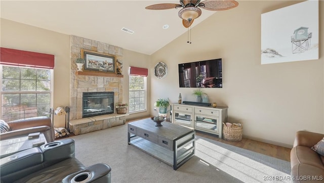 living room featuring vaulted ceiling, a wealth of natural light, a stone fireplace, and ceiling fan