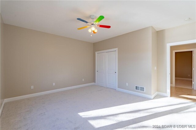 unfurnished bedroom featuring ceiling fan, light carpet, and a closet