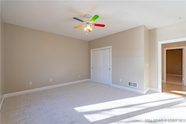 unfurnished bedroom featuring light carpet, baseboards, ceiling fan, and a closet