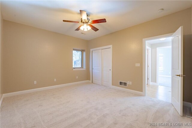 unfurnished bedroom with a closet, light colored carpet, and ceiling fan