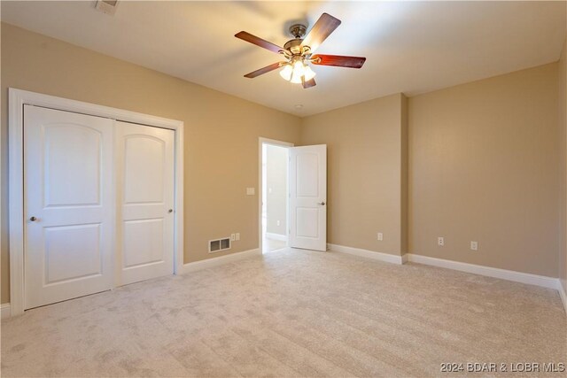 unfurnished bedroom featuring ceiling fan, light colored carpet, and a closet