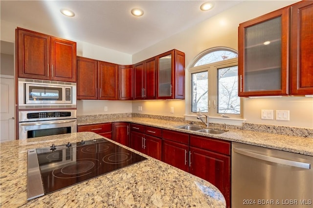 kitchen featuring stainless steel appliances, a sink, reddish brown cabinets, light stone counters, and recessed lighting