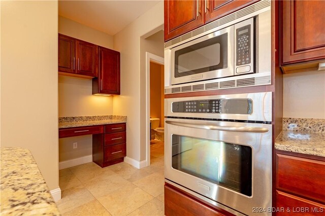 kitchen featuring light stone countertops, light tile patterned floors, built in desk, and stainless steel appliances