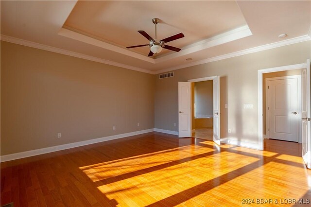 unfurnished room with a tray ceiling, hardwood / wood-style floors, and ornamental molding