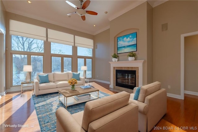 living room featuring a tile fireplace, hardwood / wood-style flooring, ceiling fan, and ornamental molding