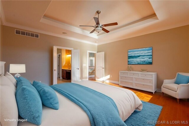 bedroom featuring a tray ceiling, connected bathroom, ceiling fan, and hardwood / wood-style flooring