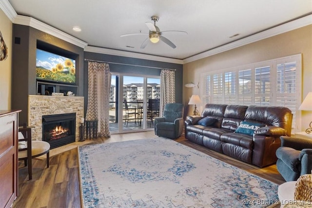 living room with ceiling fan, a stone fireplace, wood-type flooring, and crown molding