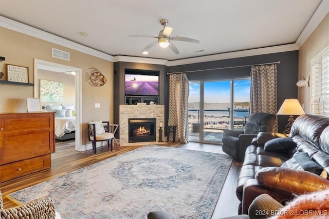 living room featuring ornamental molding, ceiling fan, a water view, light hardwood / wood-style flooring, and a stone fireplace