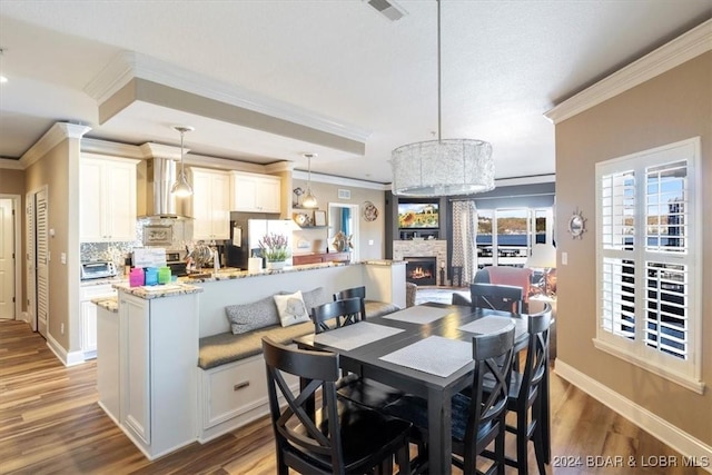 dining space featuring an inviting chandelier, hardwood / wood-style flooring, a stone fireplace, and crown molding