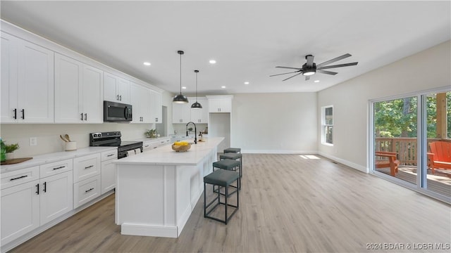 kitchen with light stone counters, electric range, decorative light fixtures, a center island with sink, and white cabinetry