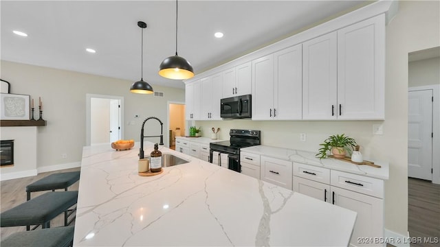 kitchen with white cabinetry, light stone countertops, hardwood / wood-style floors, a breakfast bar, and black appliances