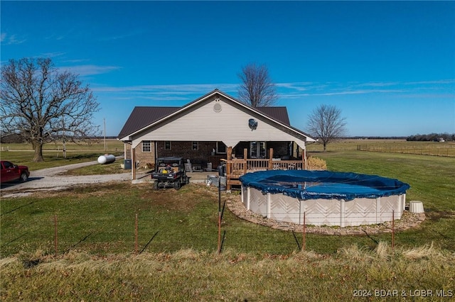 rear view of house featuring a rural view, a pool side deck, and a lawn