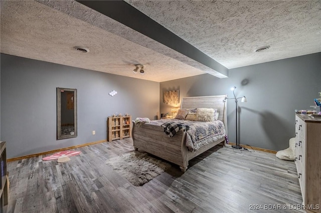 bedroom featuring beamed ceiling, light hardwood / wood-style floors, and a textured ceiling