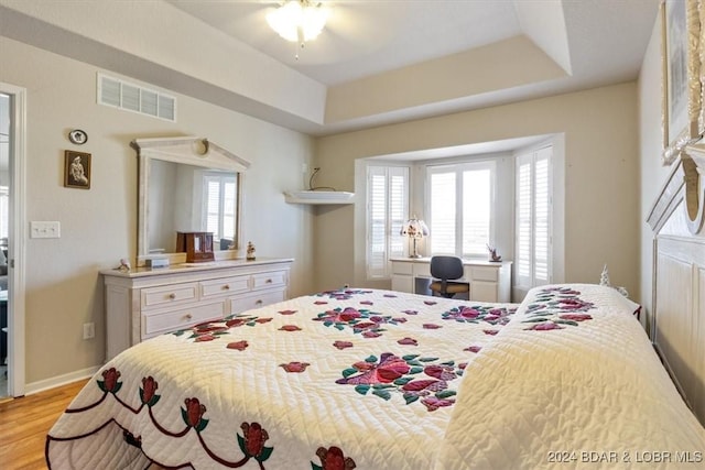 bedroom with ceiling fan, a raised ceiling, and light wood-type flooring