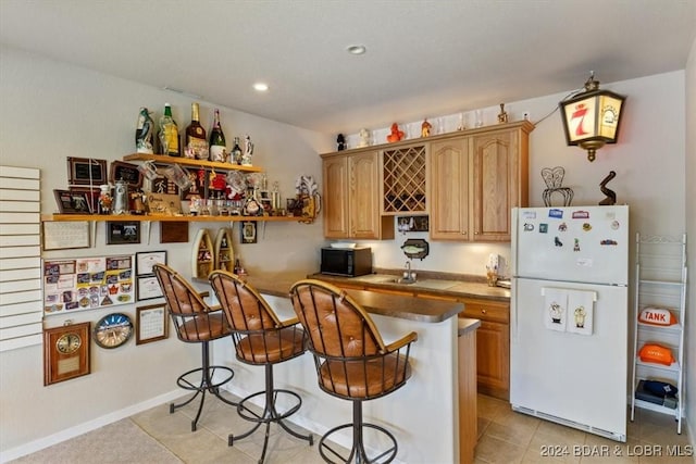 kitchen with white refrigerator, a kitchen bar, light tile patterned floors, and sink