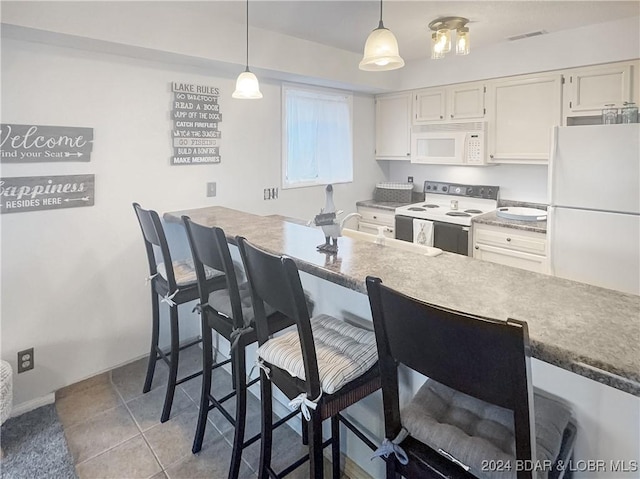 kitchen with white appliances, white cabinets, sink, hanging light fixtures, and a kitchen bar