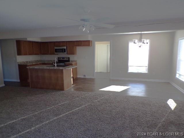 kitchen featuring appliances with stainless steel finishes, a center island with sink, dark carpet, and hanging light fixtures