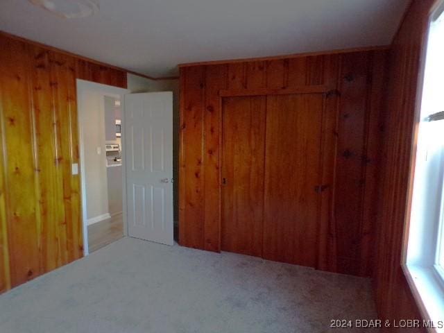 unfurnished bedroom featuring multiple windows, carpet floors, a closet, and wooden walls