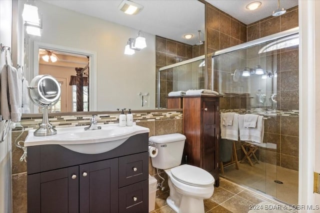 bathroom featuring tile patterned flooring, toilet, vanity, a shower with shower door, and tile walls