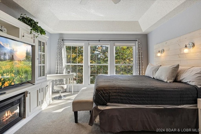 carpeted bedroom with a textured ceiling, a tray ceiling, multiple windows, and ceiling fan