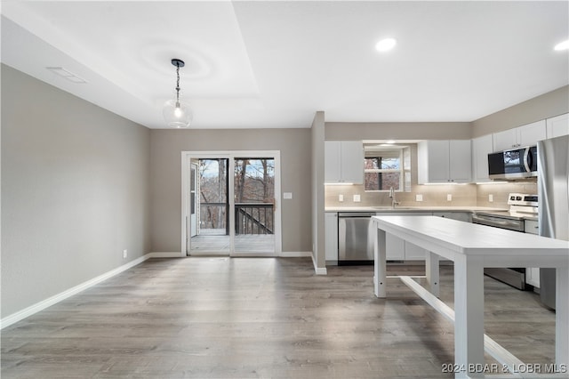 kitchen featuring hanging light fixtures, white cabinets, stainless steel appliances, and light wood-type flooring