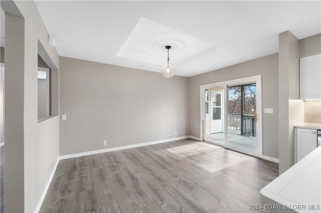 unfurnished dining area with a tray ceiling and light hardwood / wood-style flooring