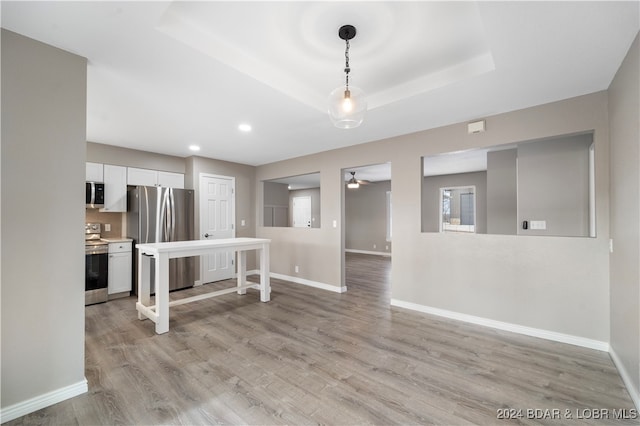 interior space featuring pendant lighting, a raised ceiling, light wood-type flooring, white cabinetry, and stainless steel appliances