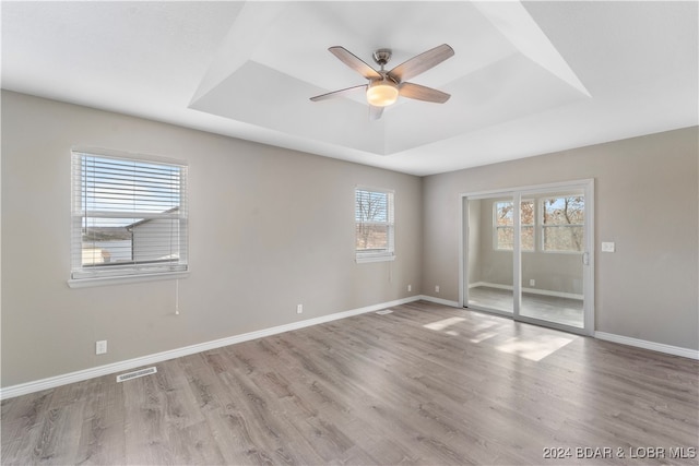 empty room featuring light wood-type flooring, a tray ceiling, and ceiling fan