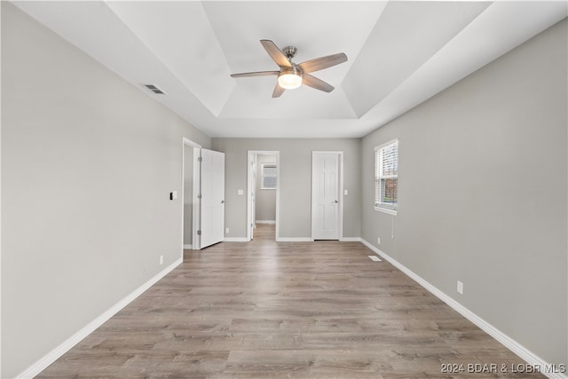 unfurnished bedroom featuring ceiling fan, a raised ceiling, and light hardwood / wood-style flooring