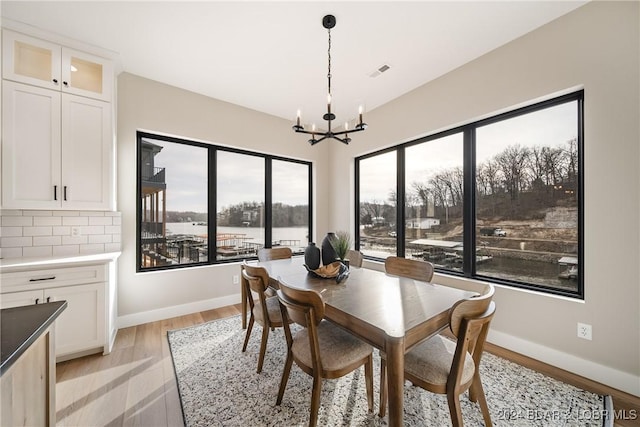 dining area featuring a water view, light wood-type flooring, and a chandelier