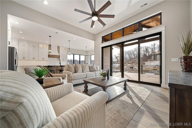 living room featuring ceiling fan with notable chandelier and light wood-type flooring