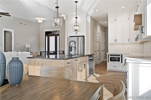 kitchen with a kitchen island with sink, white cabinets, stainless steel appliances, and decorative light fixtures