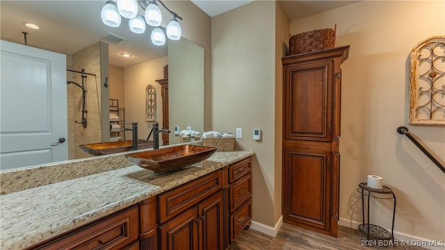 bathroom featuring wood-type flooring, a tile shower, and vanity